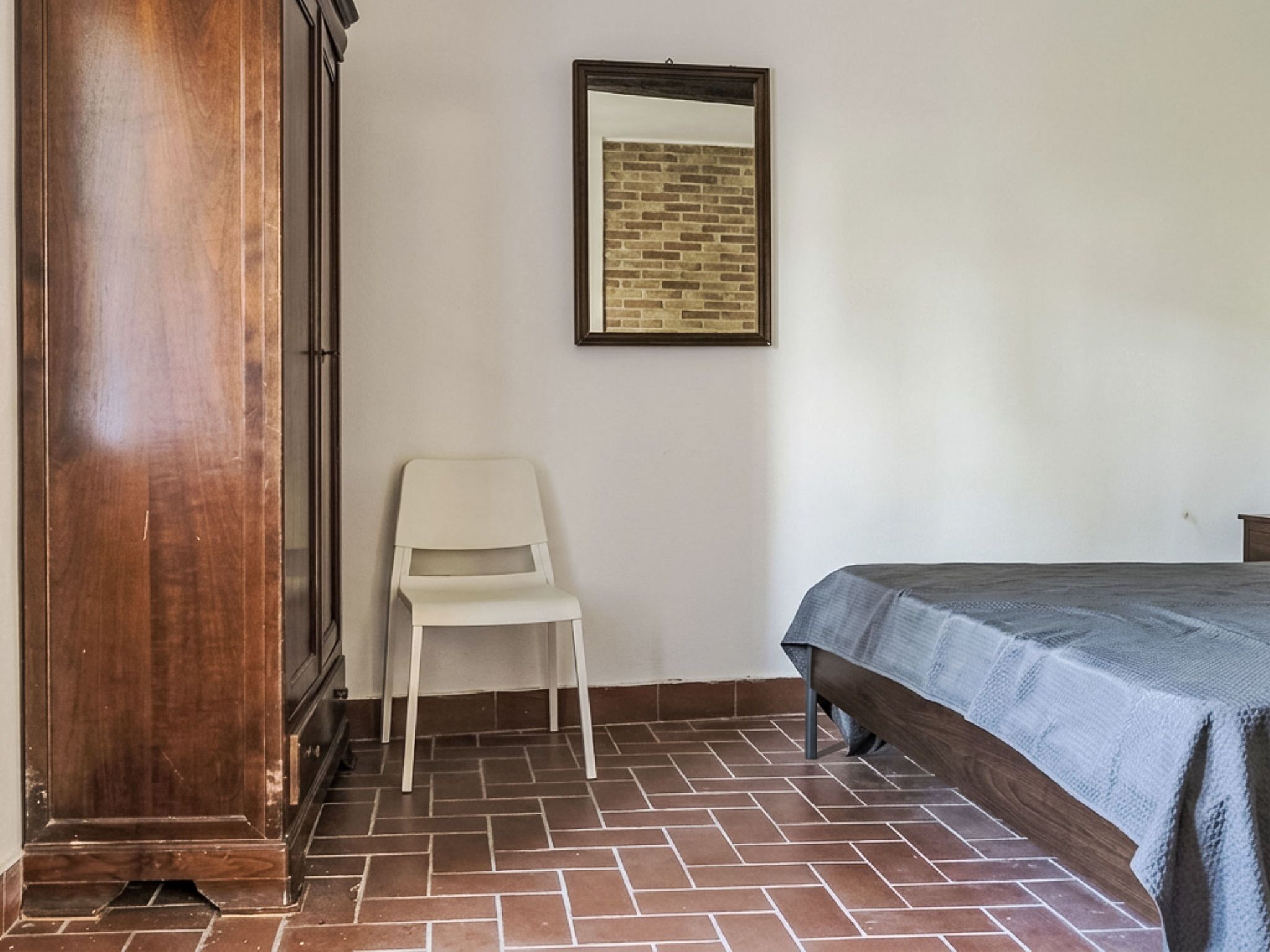 Un dormitori amb un llit, una cadira, un armari i un quadre al mur.