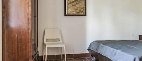 Un dormitorio con cama, una silla, un armario y un cuadro en la pared.