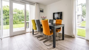 Een eetgedeelte met een tafel en stoelen, grote ramen en uitzicht op een tuin.