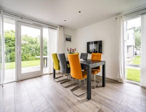 Un espace repas comprenant une table et des chaises, de grandes fenêtres et une vue sur un jardin.