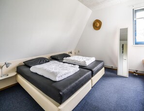 Une chambre avec deux lits, un bureau, une lampe et une fenêtre.