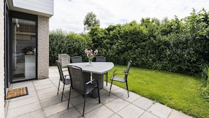 Een terras met een tafel en stoelen, een vaas met bloemen en een haag op de achtergrond.