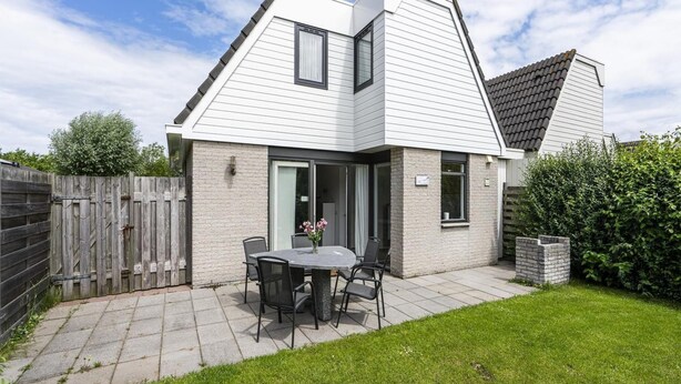Een modern huis met een terras, een eettafel met stoelen en een kleine tuin.