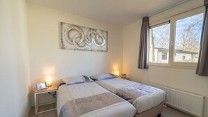 A bedroom with two beds, a large abstract painting on the wall, bedside lamps, and a window with curtains. - Pavilion L'etage Sauna 10 (Susteren)