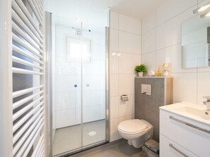 Ein modernes Badezimmer mit einer Duschkabine aus Glas, einer weißen Toilette und einem Waschtisch mit Spiegel.
