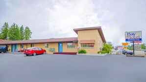 Et motel med en etage, en blå dør og en parkeringsplads med en rød bil.