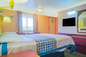 Ein Hotelzimmer mit Bett, Schreibtisch, Stuhl, einem Fenster mit Vorhängen, einem Fernseher und einem Spiegel.