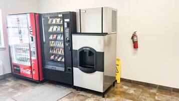 A vending machine, a push-button drink dispenser, and a fire extinguisher in a room with tiled flooring.