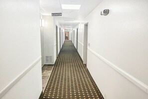 Un passadís d'hotel amb un mosaic de moqueta, parets blanques i portes a banda i banda.