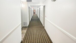 En hotellkorridor med ett mönstrat golv, vita väggar och dörrar på båda sidor.