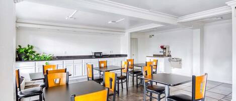 A dining area with tables and chairs, a kitchen area with appliances, and a plant.