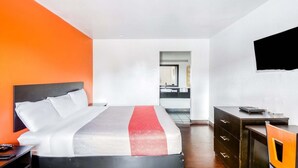 Een hotelkamer met een bed, een bureau, een stoel, een televisie en een badkamer op de achtergrond.
