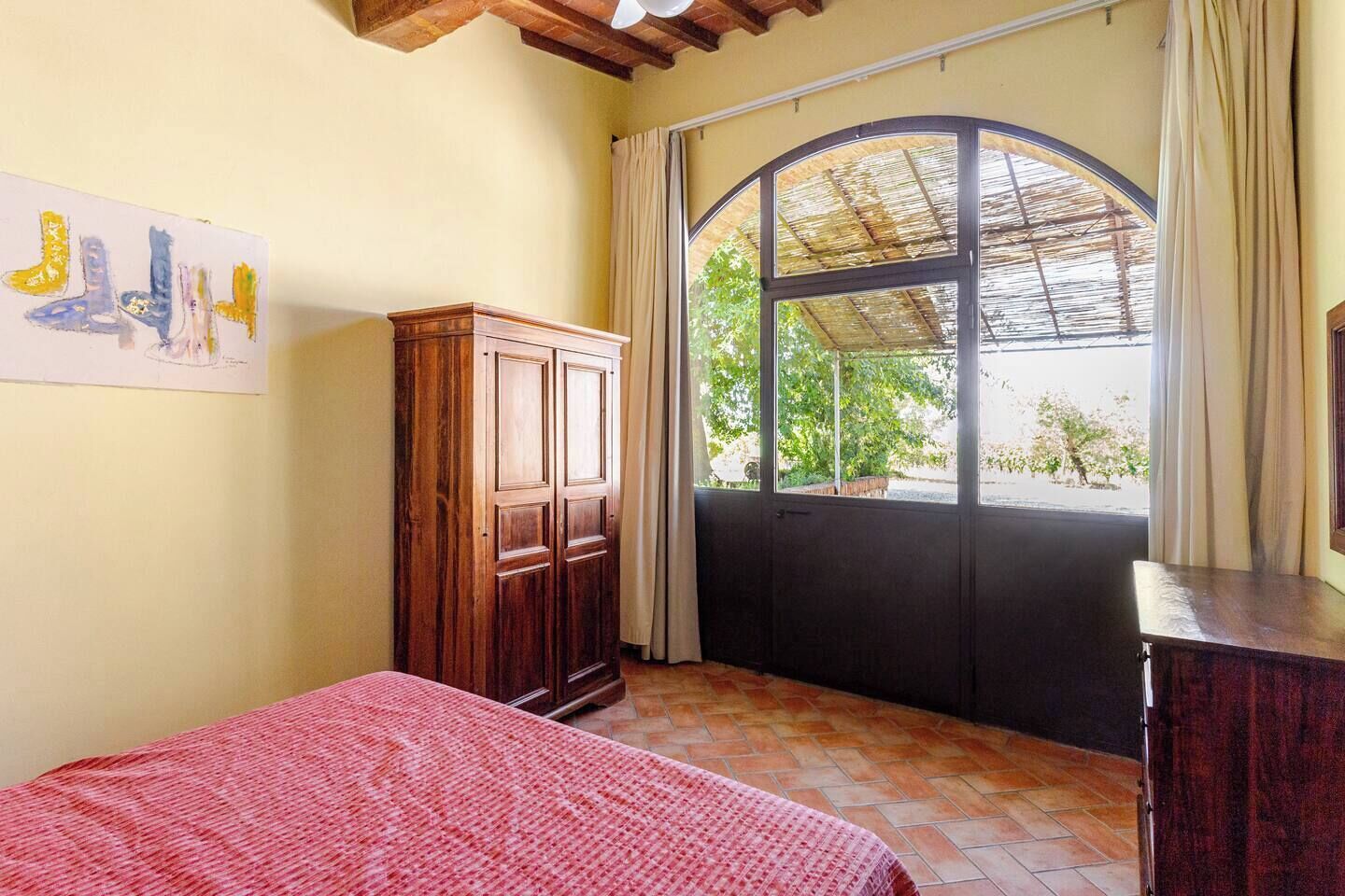 Une chambre à coucher avec un lit, une armoire en bois, une fenêtre donnant sur un paysage verdoyant et un ventilateur de plafond.