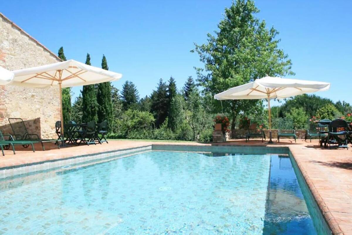 Ein Swimmingpool mit Liegestühlen und Sonnenschirmen, umgeben von Grünpflanzen und einer Steinmauer.