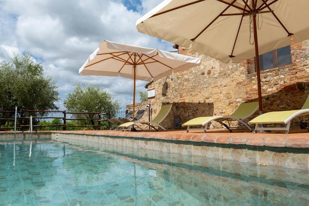 Una piscina cristalina con sillas de descanso y sombrillas, rodeada de muros de piedra y árboles.