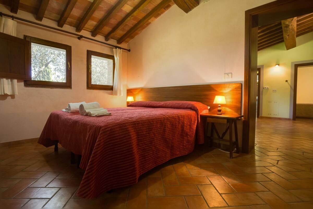 Ein Schlafzimmer mit Holzkopfteil, zwei Nachttischlampen, einem Bett mit roter Bettdecke und Holzboden.