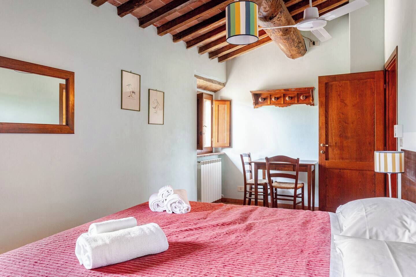 A bedroom with a bed, a desk, chairs, a radiator, and a wooden ceiling.