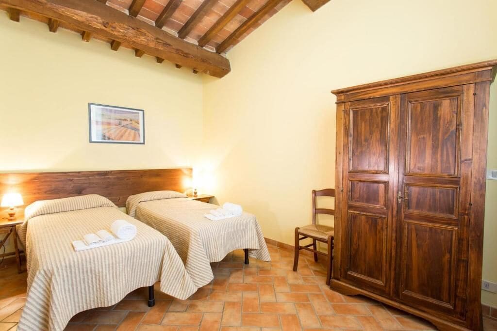 Una habitación con dos camas, un armario de madera, una silla y un cuadro en la pared.