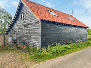 A wooden barn with a red roof, a small attached structure, and a metal gate.
