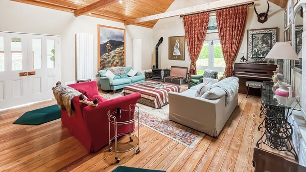 A cozy living room with wooden floors, a red armchair, a blue sofa, and a white sofa.