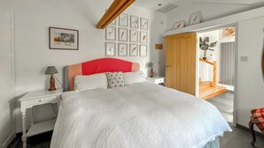 A bedroom with a large bed, a wooden wardrobe, a bedside table with a lamp, and framed pictures on the wall.