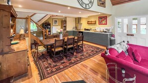 A spacious living area with a dining table, a red sofa, a large clock, and a kitchen in the background.