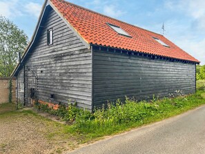 Une grange en bois avec un toit rouge, une petite dépendance attenante et un portail en métal.