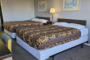 Una habitación de hotel con dos camas, un escritorio, una silla, una lámpara y dos cuadros en la pared.