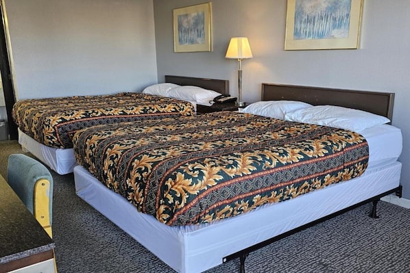 Ein Hotelzimmer mit zwei Betten, einem Schreibtisch, einem Stuhl, einer Lampe und zwei Bildern an der Wand.