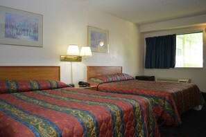 Una habitación de hotel con dos camas, una mesita de noche con lámpara, un teléfono y dos cuadros en la pared.
