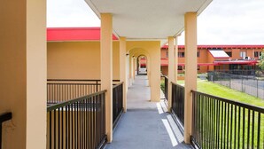 A covered corridor with yellow walls, black railings, and a red-roofed building in the background. - King Bed | Non Smoking (Doswell VA)