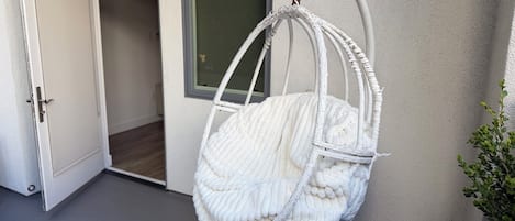 A white wicker hanging chair with a cushion, positioned against a wall near a door and a window.
