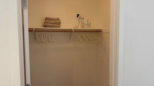 A closet with a hanging rod, a folded towel, and a hairdryer on a shelf.