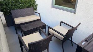 A patio with wicker furniture, including a sofa and two chairs, against a white wall with a window.