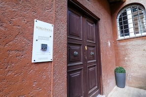 Eine braune Tür mit einem Schild, das 'BORGONOVE GUEST HOUSE' anzeigt, und einem Zahlencodefeld für den Zugang zu den Zimmern.