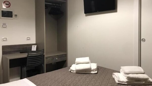 Hotellihuone, jossa on sänky, työpöytä, tuoli, seinälle asennettu televisio ja vaatekaappi.