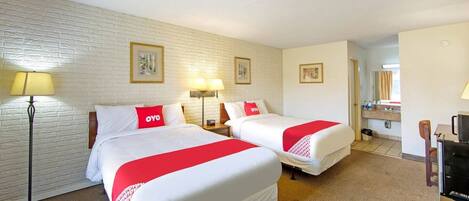 A hotel room with two beds, a flat-screen TV, a desk, and a lamp.