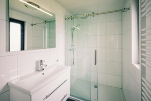 Ein modernes Badezimmer mit einer Duschkabine aus Glas, einem weißen Waschbecken und einem Spiegel darüber.