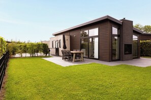 Ein modernes Haus mit Terrasse, Essbereich und Kamin aus Ziegeln.