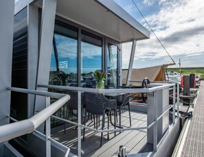 A modern deck with a glass enclosure, metal railings, and outdoor seating. - Kamperland Water Lodge (Kamperland)