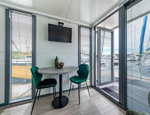 A modern room with a round table, two chairs, a television, and large windows with blinds. - Kamperland Water Lodge (Kamperland)