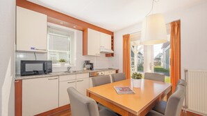 Een moderne keuken met een magnetron, fornuis en kasten. Er staat een eettafel met stoelen en een tijdschrift.