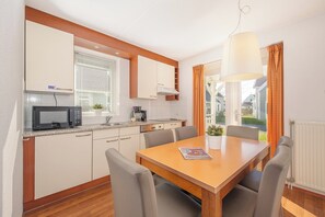A modern kitchen with a microwave, stove, and cabinets. There is a dining table with chairs and a magazine on it. - Villa Near Grevelingenmeer (Bruinisse)