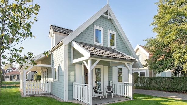 Een tweelaags huis met een veranda, een klein terras en een verzorgd gazon.