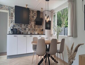 A modern kitchen with patterned tiles, a dining area with a wooden table and chairs, and a window with a view of greenery. - Stylish Chalet With Sauna in Zeeland (Heinkenszand)