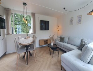 A modern living room with a dining table, sofa, and TV. - Stylish Chalet With Sauna in Zeeland (Heinkenszand)