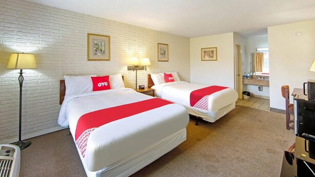 A hotel room with two beds, a flat-screen TV, a desk, and a lamp.