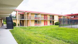 A multi-story motel with a central staircase, a fenced courtyard, and a flat roof.