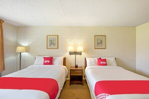 A hotel room with two beds, a nightstand with lamps, and a brick-patterned wall.