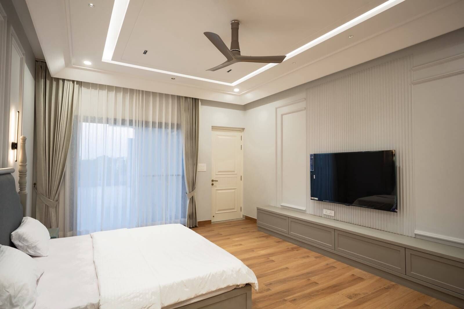 Ein Schlafzimmer mit einem Bett, einem Deckenventilator, einem an der Wand montierten Fernseher und einer Tür.